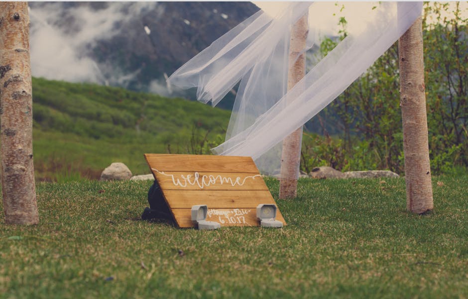 Whitewashed wooden wedding welcome sign at an outdoor ceremony surrounded by greenery