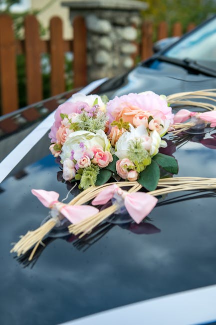 White wedding car with a floral arrangement and trailing ribbons showing floral wedding car decoration ideas