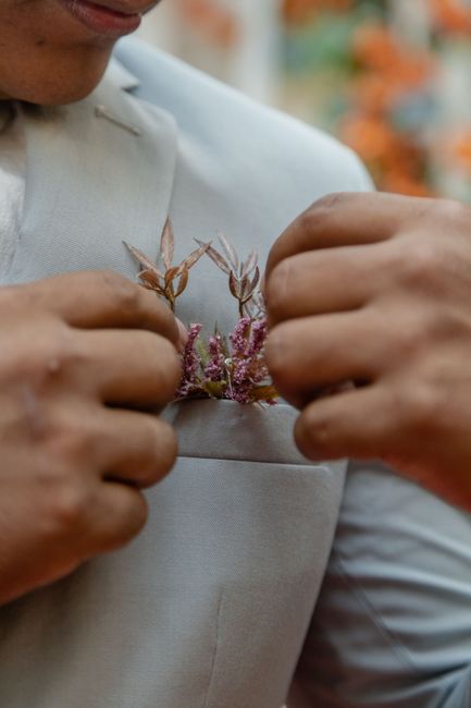 Close-up of hands pinning a boutonniere onto a wedding suit lapel