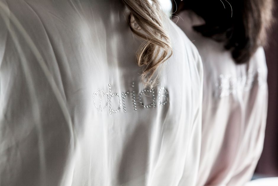 Close-up detail of a white satin bride robe with monogram embroidery