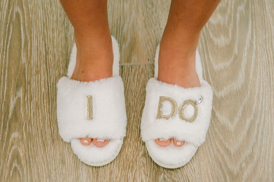 White fuzzy bride slippers for wedding morning getting ready flatlay photo