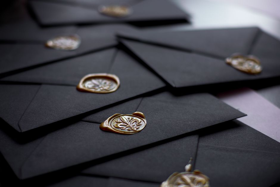 Gold wax seal stamp being pressed onto wedding invitation envelope